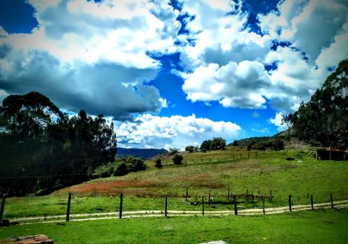 ein Grasfeld mit einem Zaun und einem blauen Himmel mit Wolken in der Unterkunft Villas de Sanjuan in Suesca