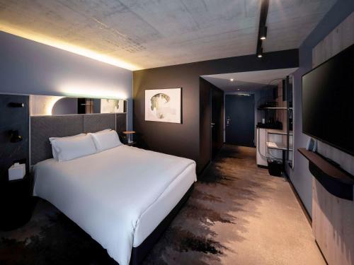 a bedroom with a large white bed and a flat screen tv at Mercure Hotel Delémont in Delémont