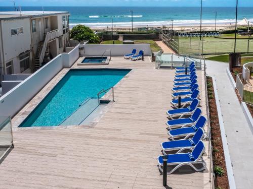a row of blue lounge chairs next to a swimming pool at Breakers North Absolute Beachfront Apartments - Official in Gold Coast