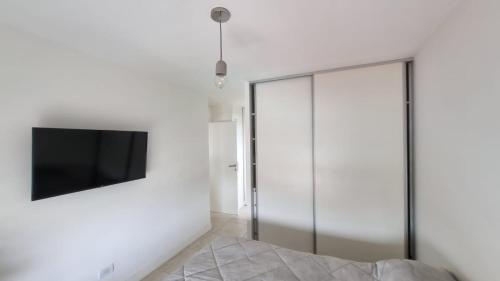Messidor Mar del Plata Luminoso departamento 2 ambientes con cochera في مار ديل بلاتا: غرفة نوم بأبواب زجاجية وجهاز تلفزيون على الحائط