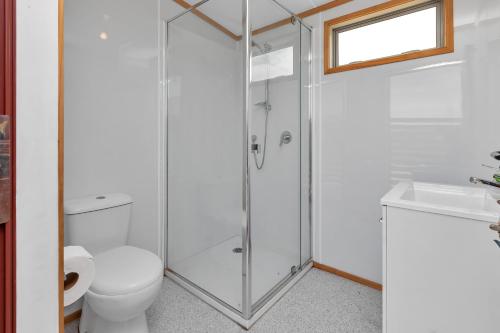 a bathroom with a shower and a toilet and a sink at Karo Hut B - Ninety Mile Beachfront Cabin in Awanui