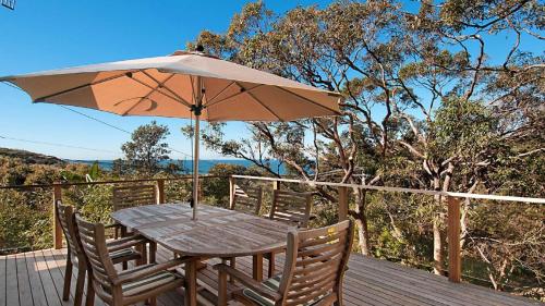 a wooden table with an umbrella on a deck at 'Charming Cottage Retreat' by HolidayCo in Killcare