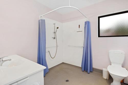 a bathroom with a toilet and a shower with blue curtains at Rose Cottage - Lake Coleridge Holiday Home in Lake Coleridge