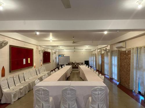 uma sala de conferências com mesas e cadeiras brancas e um ecrã em River Park International Resort em Chitwan