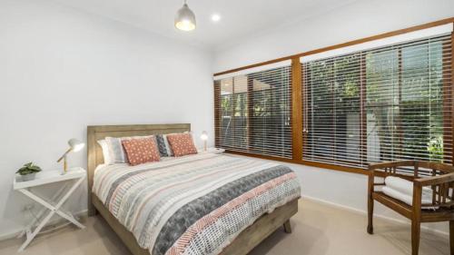 a bedroom with a bed and a chair and windows at Pearl Beach Quarterdeck in Pearl Beach