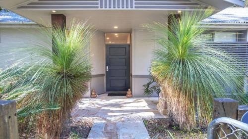 a house with two palm trees in front of a door at Waters Edge - Pet Friendly Holiday Home in Pearl Beach