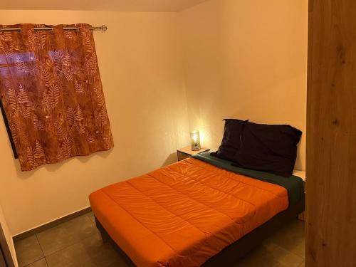 1 dormitorio con 1 cama con manta naranja y ventana en KOM LA KAZ en Cilaos