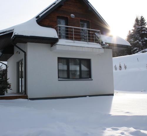 ein Haus mit Schnee auf dem Boden davor in der Unterkunft Panskiemisie Domki Całoroczne sauna jacuzzi in Wetlina
