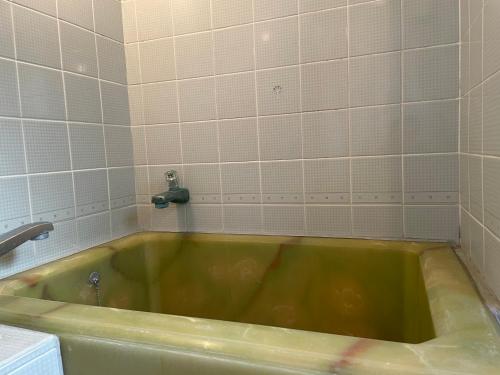 a green bath tub in a bathroom with white tiles at 素泊まり宿　瑞宝荘 in Atami