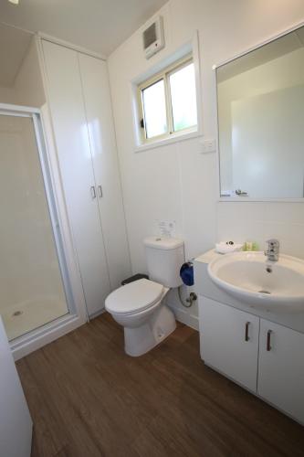 a white bathroom with a toilet and a sink at Kanasta Caravan Park in Rye