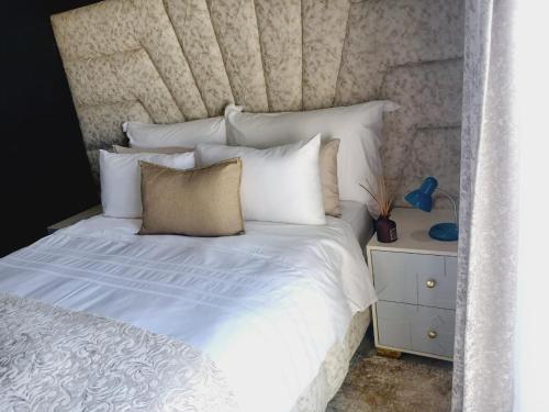 a bed with white sheets and pillows next to a night stand at Danko baba guest house & etc. in Welkom