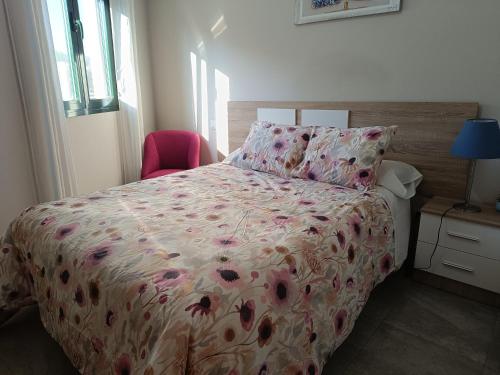 a bedroom with a bed with a floral comforter and a chair at EL BOSQUE 1 - Parking gratis in Toledo