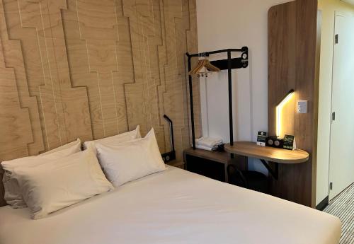 un letto con lenzuola e cuscini bianchi in una stanza di B&B HOTEL Cergy Saint-Christophe Gare a Cergy