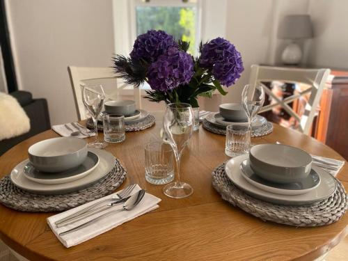 a wooden table with plates and glasses and purple flowers at Knockfarrie Cottage in Pitlochry