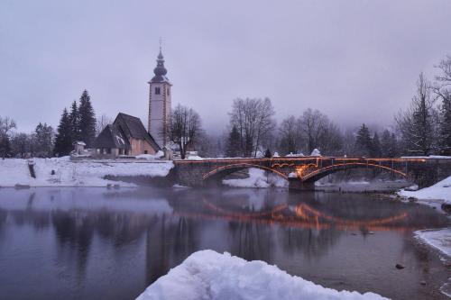 un puente sobre un río con una iglesia y una torre del reloj en Hotel Jezero, en Bohinj