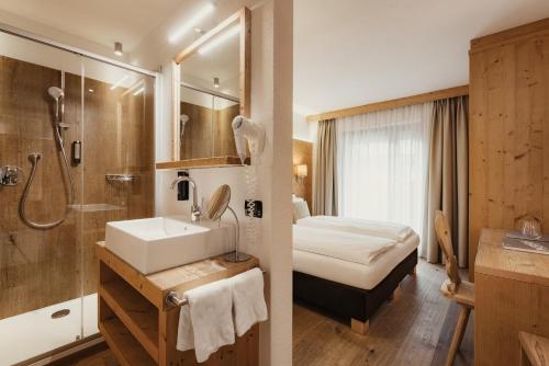 a bathroom with a sink and a shower and a bed at Diana Dolomites Living & Taste in La Villa