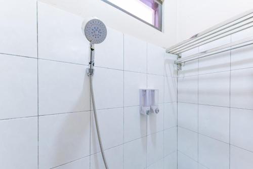 a shower with a shower head in a white tiled bathroom at RedDoorz Syariah near Exit Toll Subang in Subang
