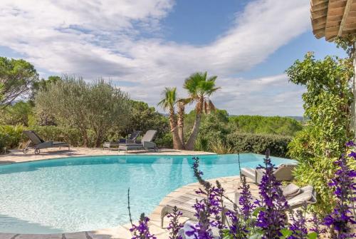 - une piscine avec des chaises, des arbres et des fleurs violettes dans l'établissement Le Mas de Héron, à Vidauban
