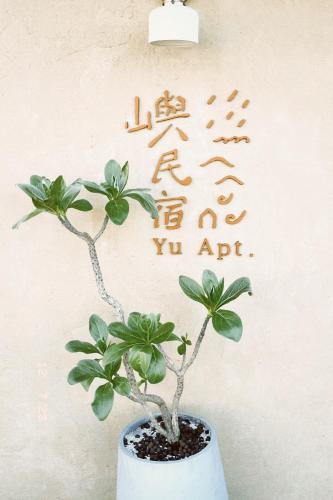 a plant in a white vase with writing on the wall at Yu Apartment in Jiufen