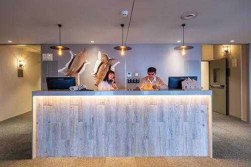 two people standing at a counter in an office at Apartamentos Caribou in Pas de la Casa