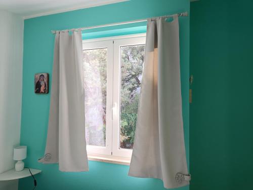 okno z białymi zasłonami w niebieskim pokoju w obiekcie Appartamento Sole w mieście Cala Gonone