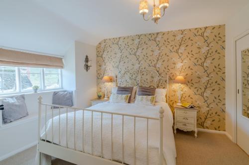 a bedroom with a white bed with a floral wallpaper at Red Lion Cottage in Blockley