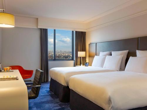una camera d'albergo con due letti e una sedia rossa di Pullman Paris Montparnasse a Parigi