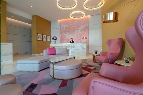un salon avec des chaises roses et une femme en arrière-plan dans l'établissement Hilton Dubai Creek Hotel & Residences, à Dubaï