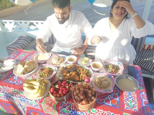 a man and a woman sitting at a table with food at Aswan Felucca sailing boat and Hotel in Aswan