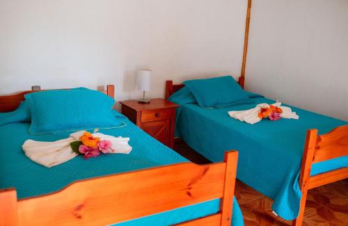 twee bedden in een kamer met blauwe lakens en bloemen erop bij Cabañas Vaiora in Hanga Roa