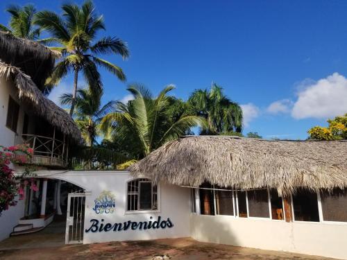 a white building with a straw roof and palm trees at Jardín del Coco in Las Galeras