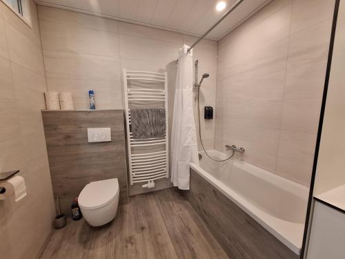 a white bathroom with a toilet and a bath tub at Alpenview Apartments Hauser in Reisach