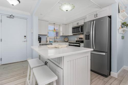 La cuisine est équipée de placards blancs et d'un réfrigérateur en acier inoxydable. dans l'établissement Beach Villas #401 - 250 Estero Blvd condo, à Fort Myers Beach