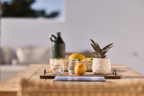 a wooden table with two glasses and a potted plant at Villa Manikas Milos in Adamas