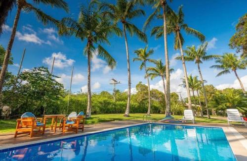 a pool with chairs and a table and palm trees at Casa Trancoso Refúgio in Trancoso
