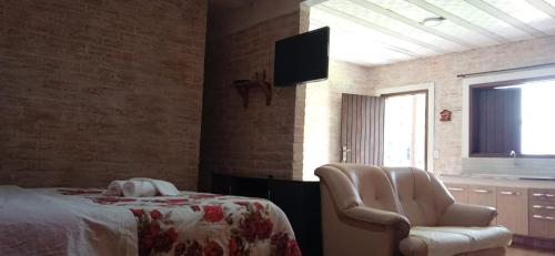 a bedroom with a bed and a chair and a tv at Chalé das Orquídeas in Monte Verde