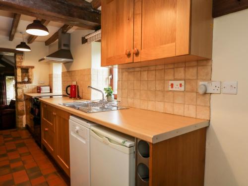 a kitchen with wooden cabinets and a white dishwasher at Stable Cottage in Moreton in Marsh