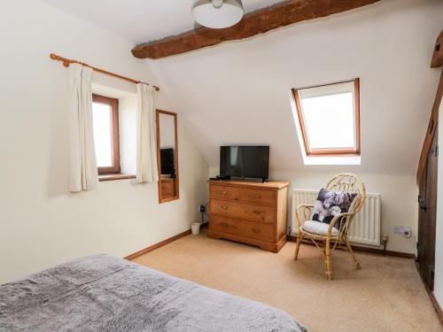 a bedroom with a bed and a tv and a chair at Stable Cottage in Moreton in Marsh