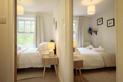 two beds in a bedroom with two lamps and a mirror at Meadow View - Cosy townhouse with patio garden & parking in Kendal