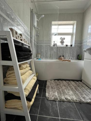 a bathroom with a bath tub and a shelf with towels at Rose Garden Retreat in Rayleigh