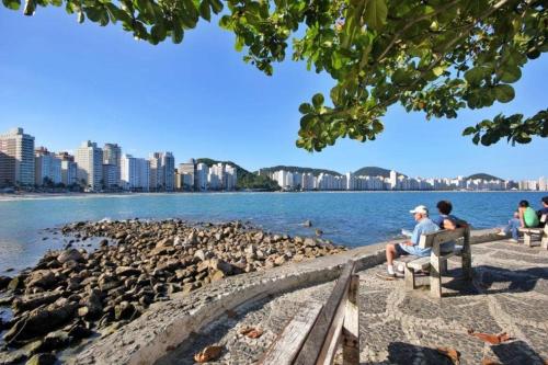 a group of people sitting on a bench by the water at Apartamento Na Praia Das Astúrias in Guarujá