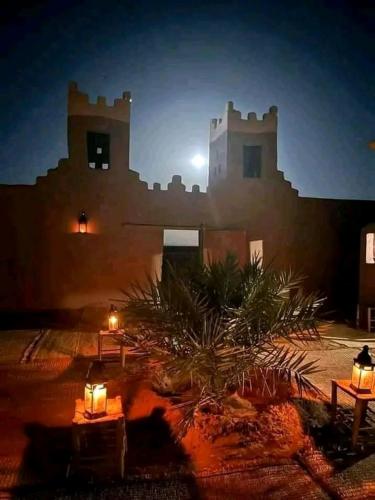 a building with lights and a palm tree in front of it at AUBERGE SAHARA IRIKI & Désert Tours in Foum Zguid