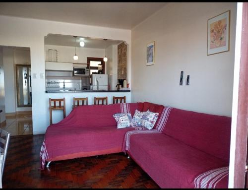 a red couch in a living room with a kitchen at Apartamento Paraíso A Beira Mar in Torres