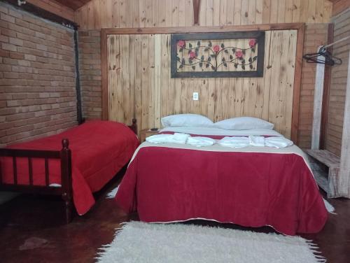 a bedroom with two beds with red sheets and a brick wall at Pousada Toque de Minas in Visconde De Maua