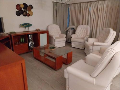 uma sala de estar com cadeiras brancas e uma mesa de centro em Apartamento frente al Mar para 7 em Pinamar