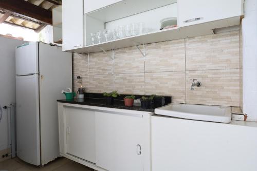 La cuisine est équipée de placards blancs, d'un évier et d'un réfrigérateur. dans l'établissement Suítes Praia dos Anjos - Arraial do Cabo, à Arraial do Cabo
