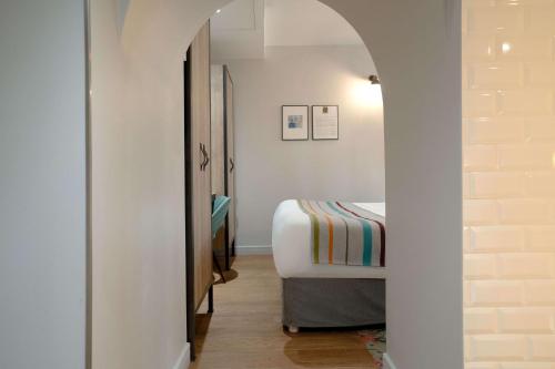 a small bedroom with a bed and a hallway at Hotel Litteraire Marcel Ayme, BW Premier Collection in Paris