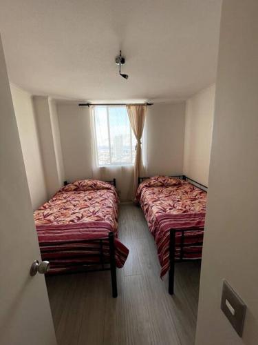 two beds in a small room with a window at Arriendo departamento Amunategui in Iquique