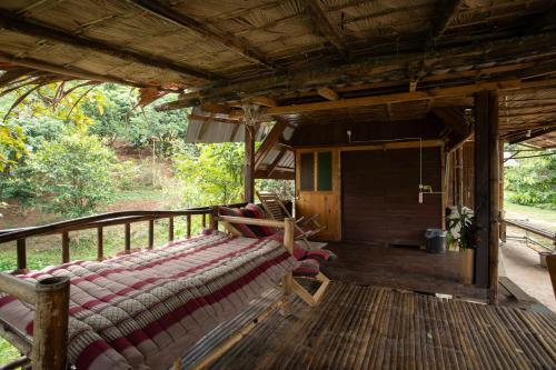 a porch of a house with a bed on a deck at Khaokhopimphupha farmstay เขาค้อพิมภูผาฟาร์มสเตย์ ไม่มีไฟฟ้า น้ำจากน้ำตกธรรมชาติ Low cabon with Sustainability cares in Ban Non Na Yao