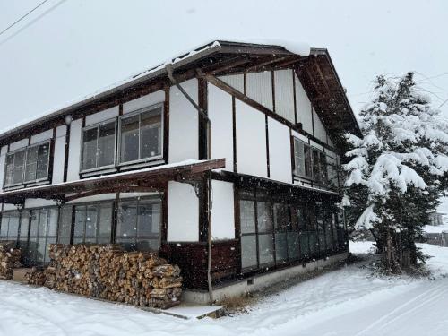 a house with a pile of logs in the snow at 白馬の黒馬　DarkHorse @Hakuba in Hakuba